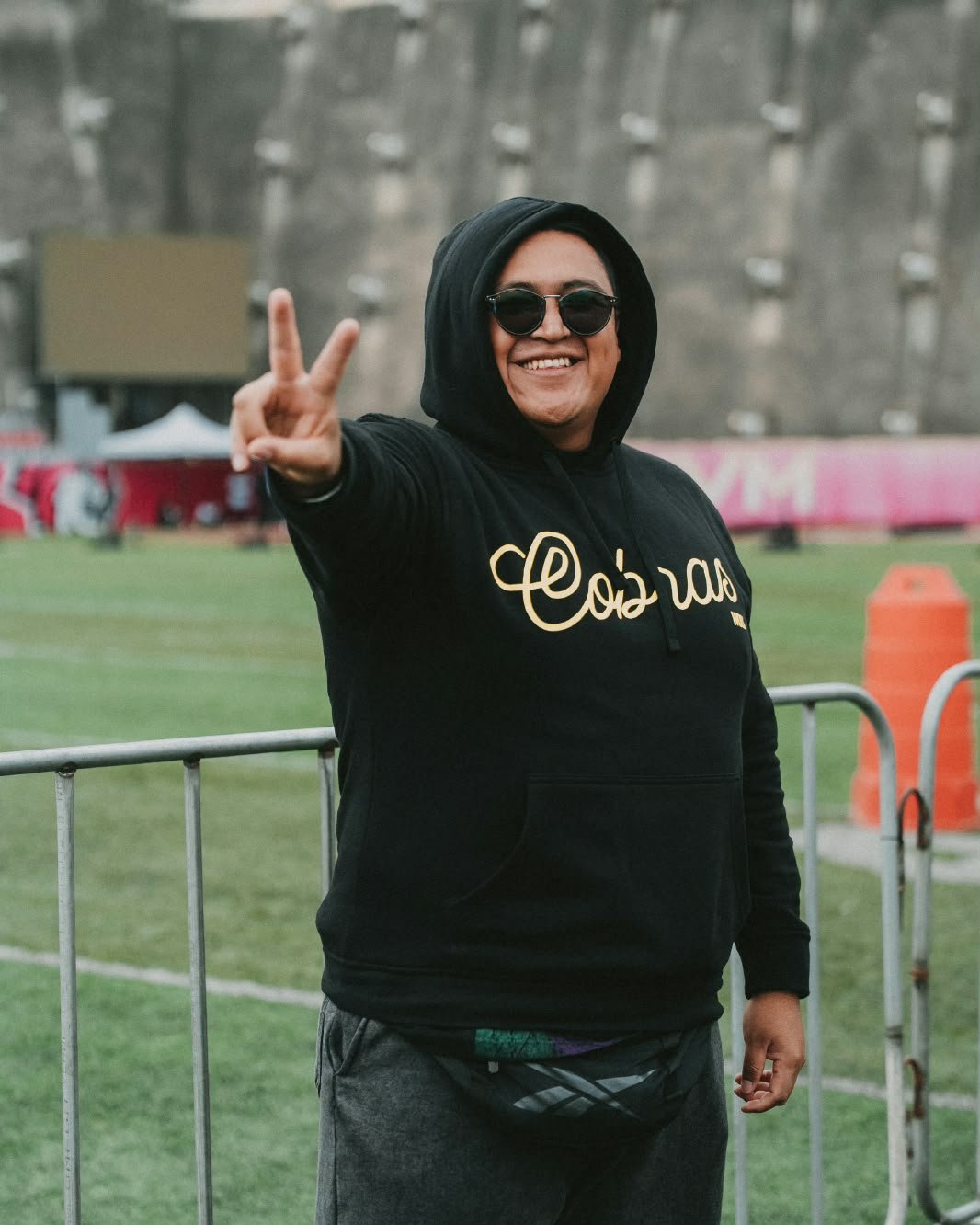 Charly Cam en un evento deportivo, sonriendo y haciendo la señal de paz