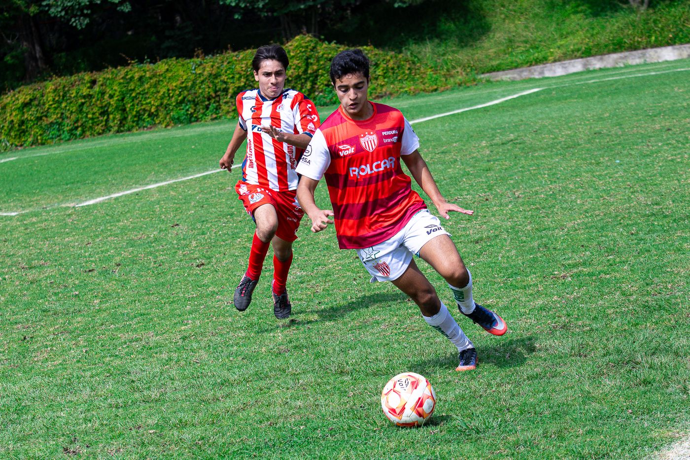 Jugador avanzando con el balón perseguido por un rival