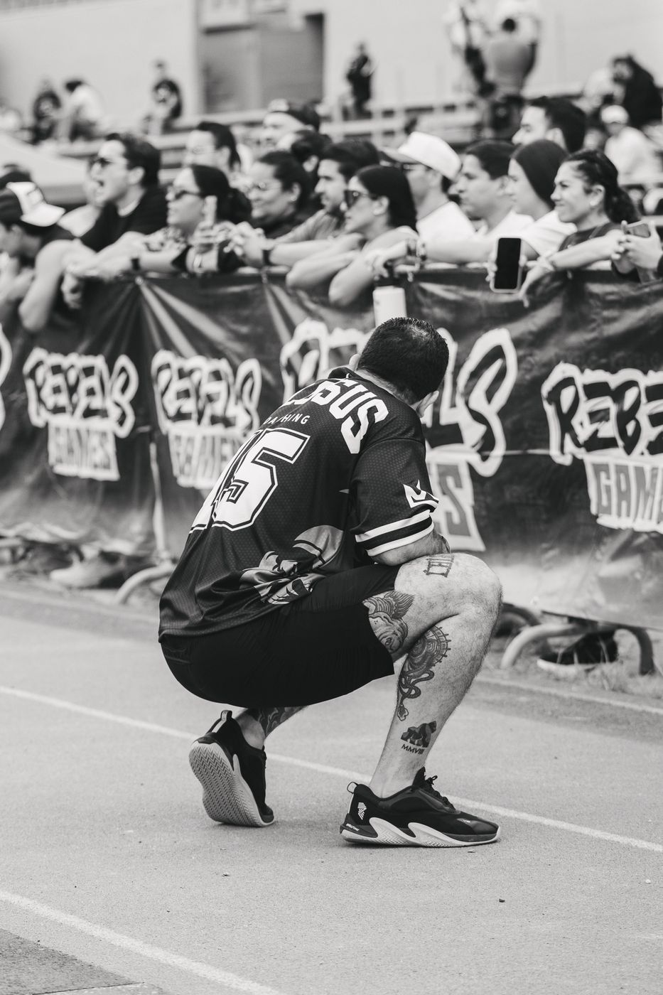 Atleta en cuclillas recuperando el aliento junto a la barda de la competencia, en blanco y negro
